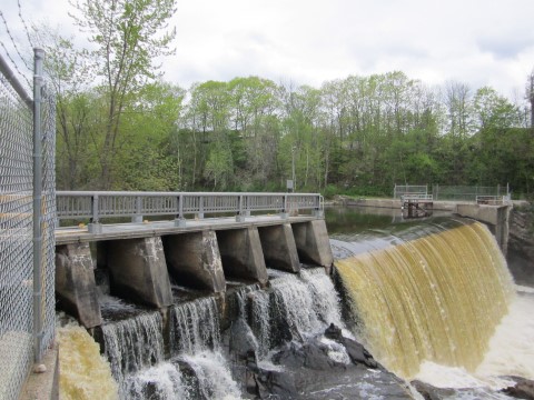 Water flowing over the Lower Barker Hydro Dam, trees in the background.